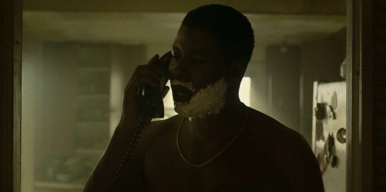 They Cloned Tyrone (2023) movie still: medium — A man stands in an apartment doorway with shaving cream on his face. He is shirtless and holds a…