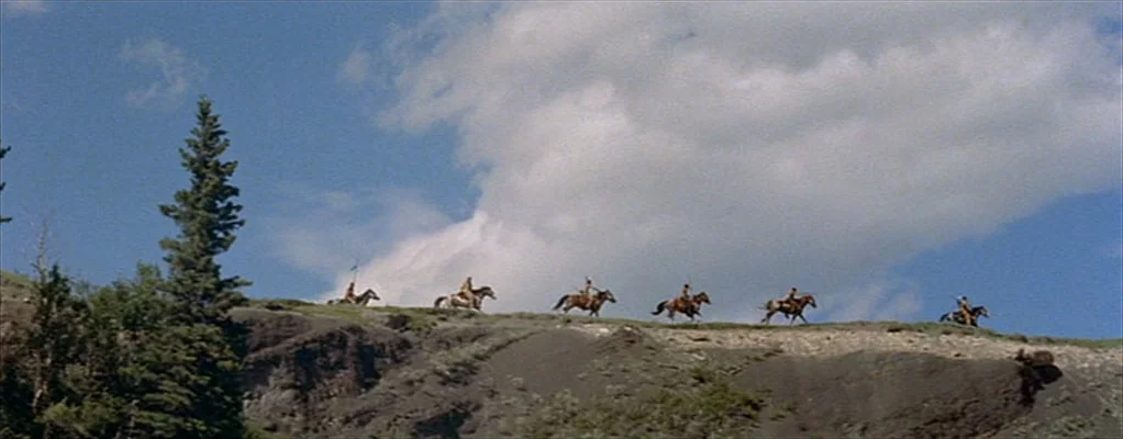 River of No Return (1954) movie still: wide — A row of horseback riders travels along the crest of a grassy rocky hill. They appear as small…