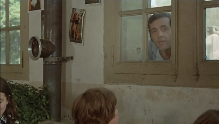 Le Boucher (1970) movie still: medium — A classroom wall features a dark metal pipe and several small paper photos taped up. A man looks in from…