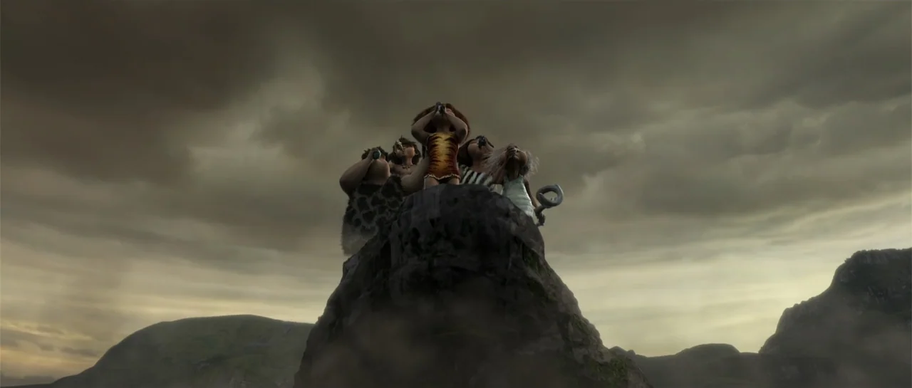 The Croods (2013) movie still: fullbody — A prehistoric family stands on a large rocky formation against a dark, overcast sky. The five figures look…