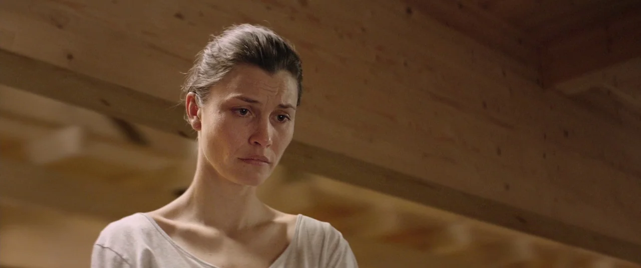 Force Majeure (2014) movie still: closeup — A woman stands indoors against a wooden ceiling beam structure. She looks down with a furrowed expression.