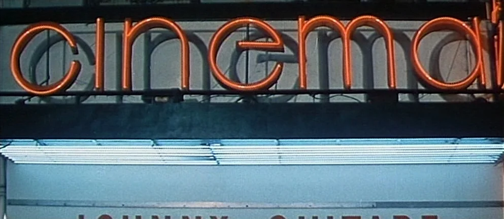 Mississippi Mermaid (1969) movie still: closeup — A close-up shot of a theater marquee with bright orange neon letters. The word cinema glows atop a…