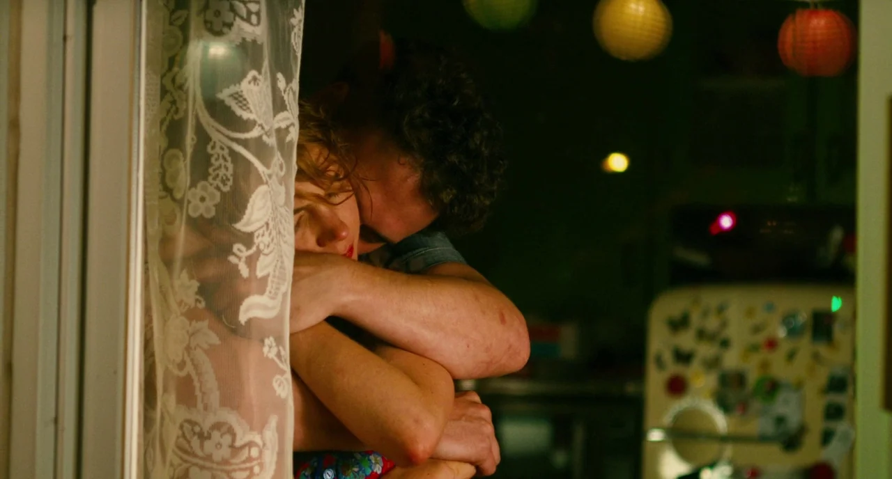 Take This Waltz (2011) movie still: closeup — An interior space features a lace curtain in the foreground near the subjects. A man and a woman…