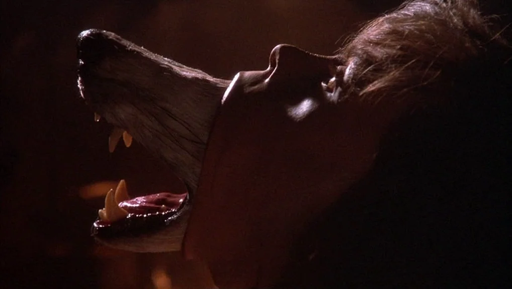 The Company of Wolves (1984) movie still: closeup — A dark space provides the backdrop for a physical transformation. A human face stretches into a…