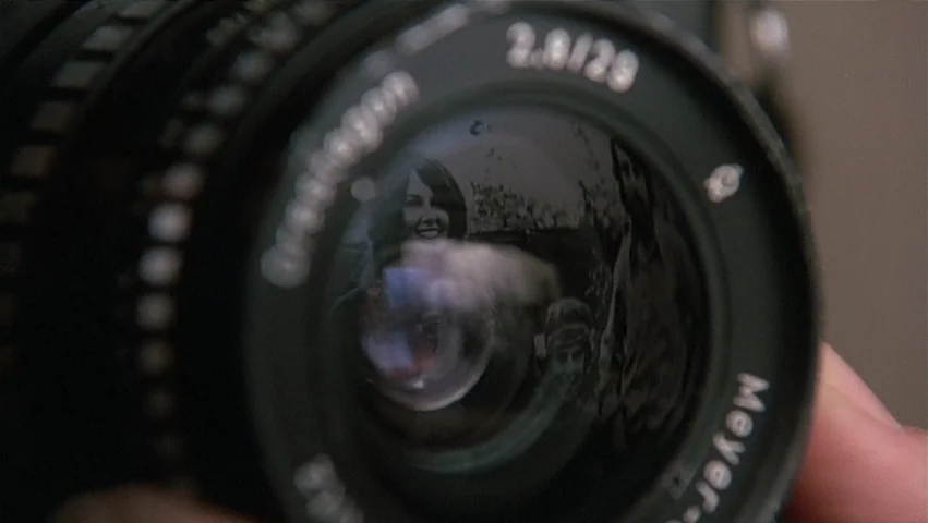 The Unbearable Lightness of Being (1988) movie still: closeup — A close-up view shows a black manual camera lens held in someone's hand. The glass…