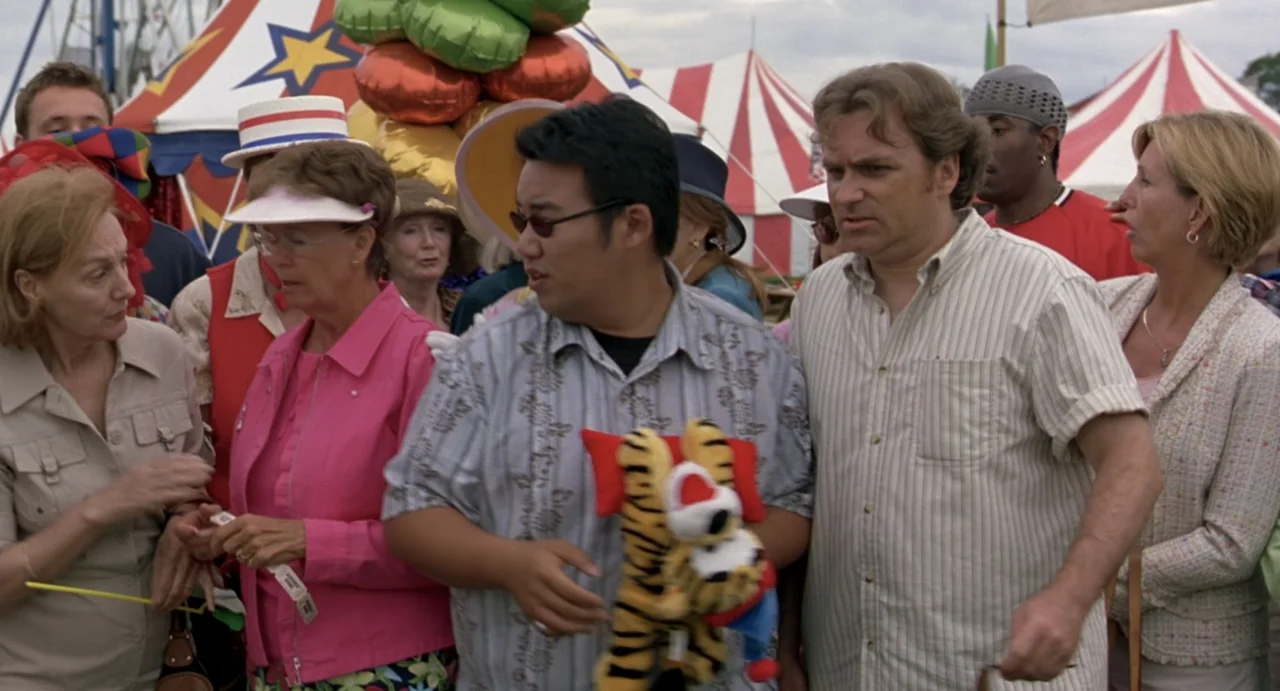 She's the Man (2006) movie still: medium — A group of people navigate a crowded carnival setting with red and white tents. Several individuals walk…