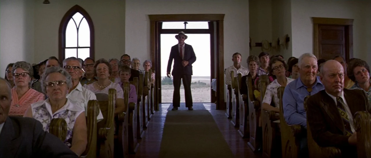 Thunderbolt & Lightfoot (1974) movie still: wide — A rural church interior features rows of wooden pews filled with seated individuals. A man in a…