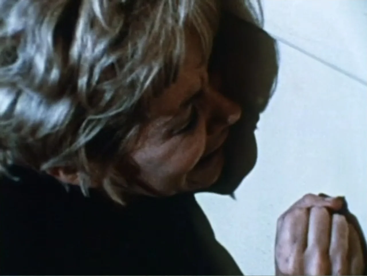 It's Alive (1974) movie still: closeup — A corner of an interior room with a plain, off-white wall surface. A woman leans her side against the wall…