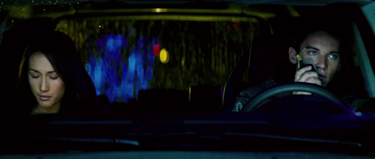 Mission: Impossible III (2006) movie still: medium — Two individuals sit in the front seats of a dark vehicle at night. Rain streaks across the…