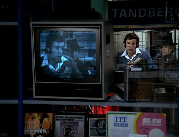 The Arrival of Joachim Stiller (1976) movie still: medium — A cluttered electronics store window display features a Sony television broadcasting a…