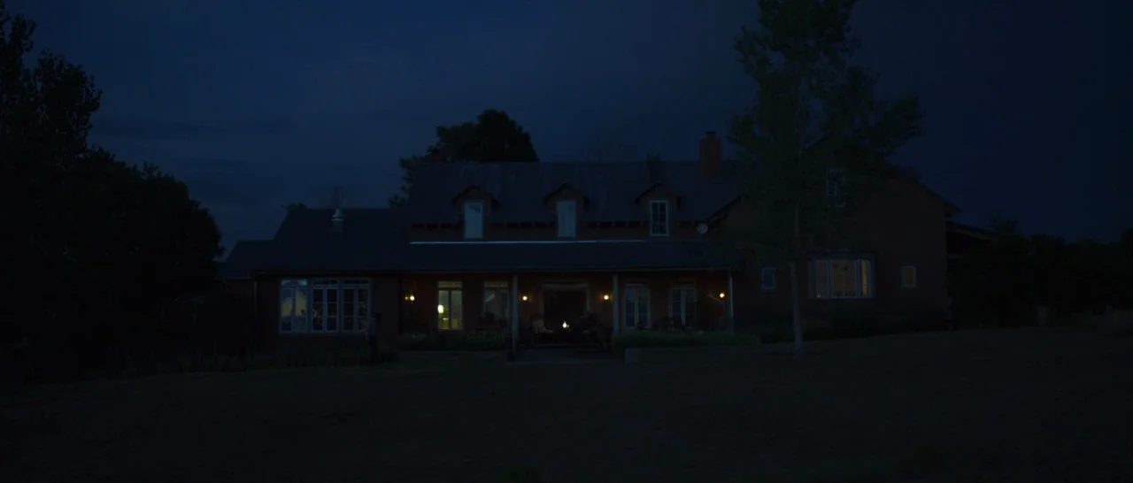 Only The Brave (2017) movie still: establishing — A two-story farmhouse sits on a dark hillside at night under a clear sky. Several windows and an…