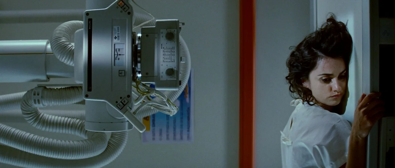 Broken Embraces (2009) movie still: medium — An interior medical diagnostic room with a large overhead X-ray machine and white walls. A woman in a…