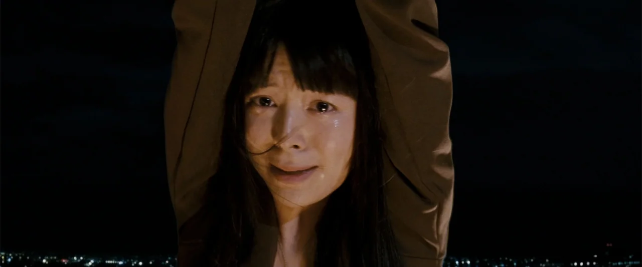 Rush Hour 3 (2007) movie still: closeup — An exterior rooftop at night overlooks a distant city skyline under a dark sky. A woman stands with her…