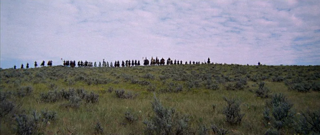 Little Big Man (1970) movie still: wide — A vast, grassy hillside covered in low sagebrush stretches under a wide cloudy sky. A long line of…