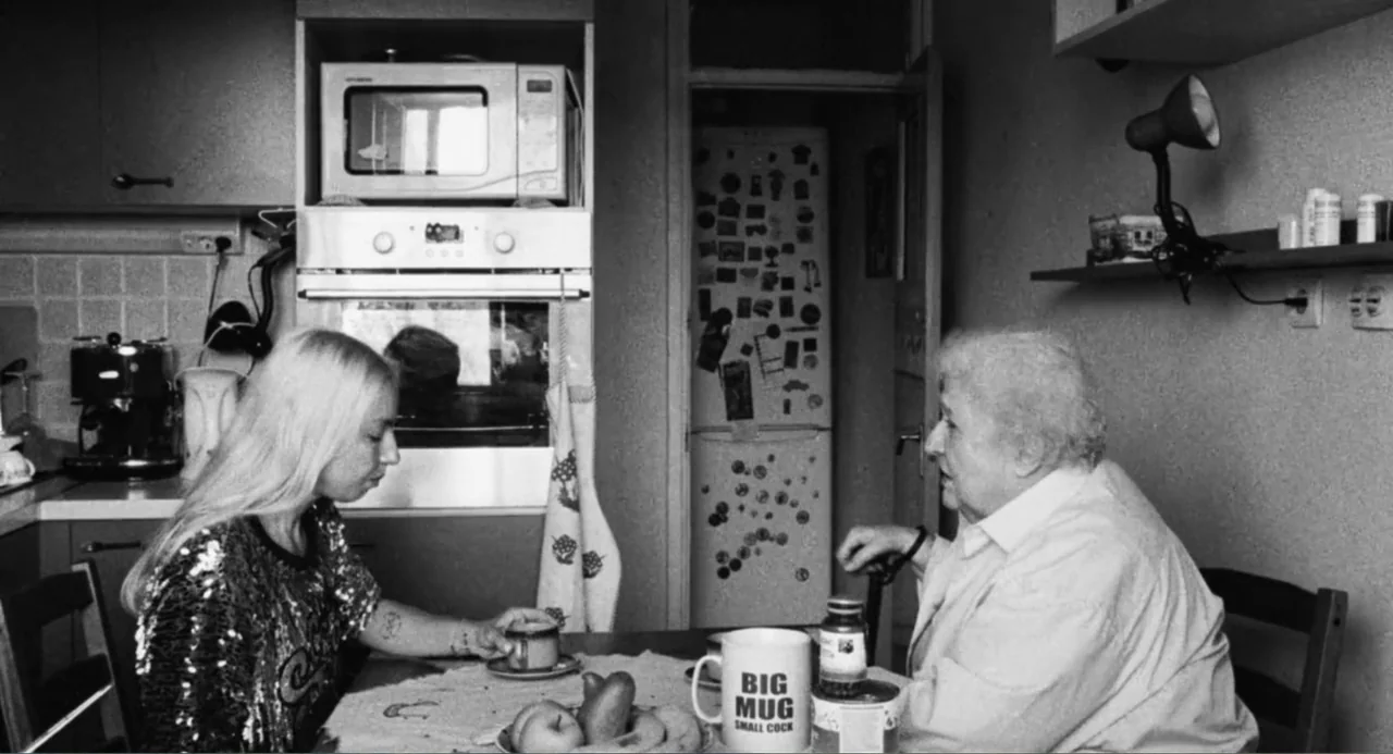 Do Not Expect Too Much from the End of the World (2023) movie still: medium — A modest domestic kitchen features a dining table, microwave, and…
