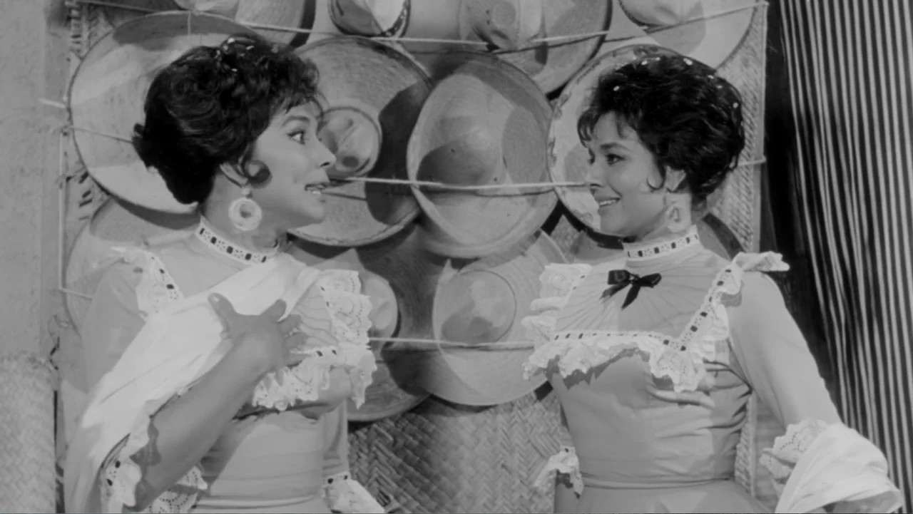 Escuela para solteras (1965) movie still: medium — An interior wall covered with woven straw hats displayed as a backdrop. Two women wearing ruffled…