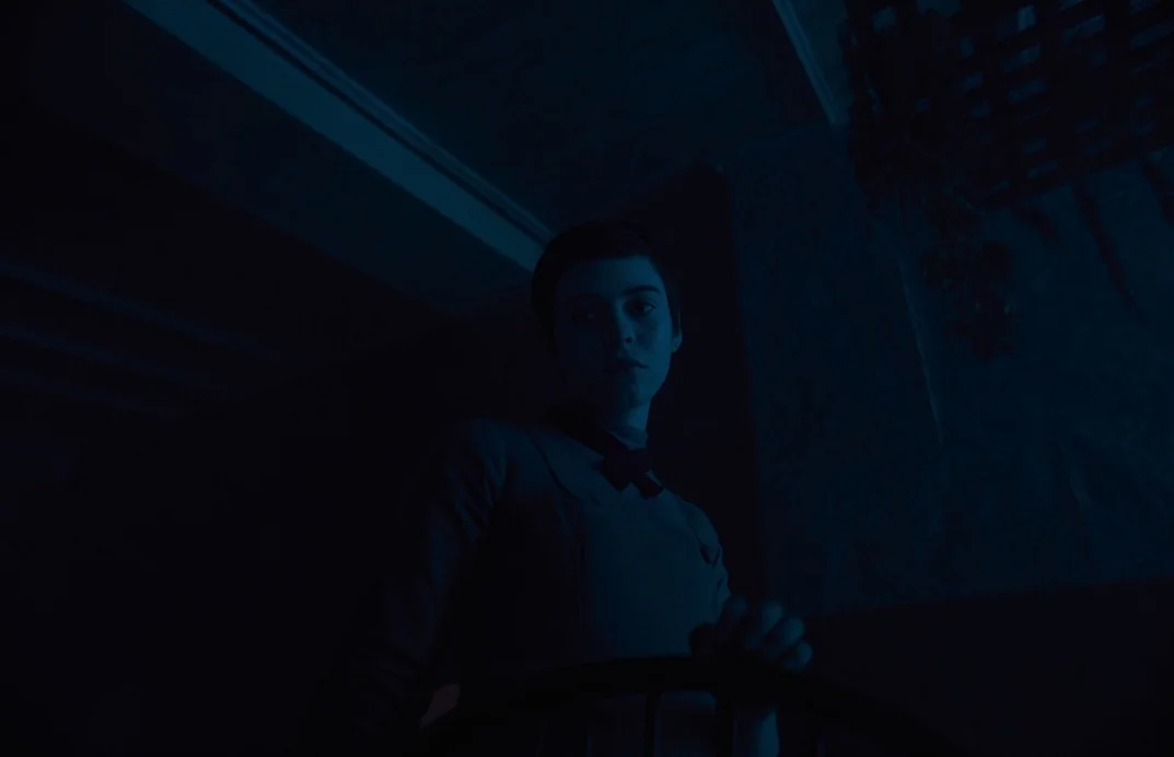 Gretel & Hansel (2020) movie still: medium — A dimly lit room with blue shadows and a dark wooden chair. A young woman with short hair stands in the…