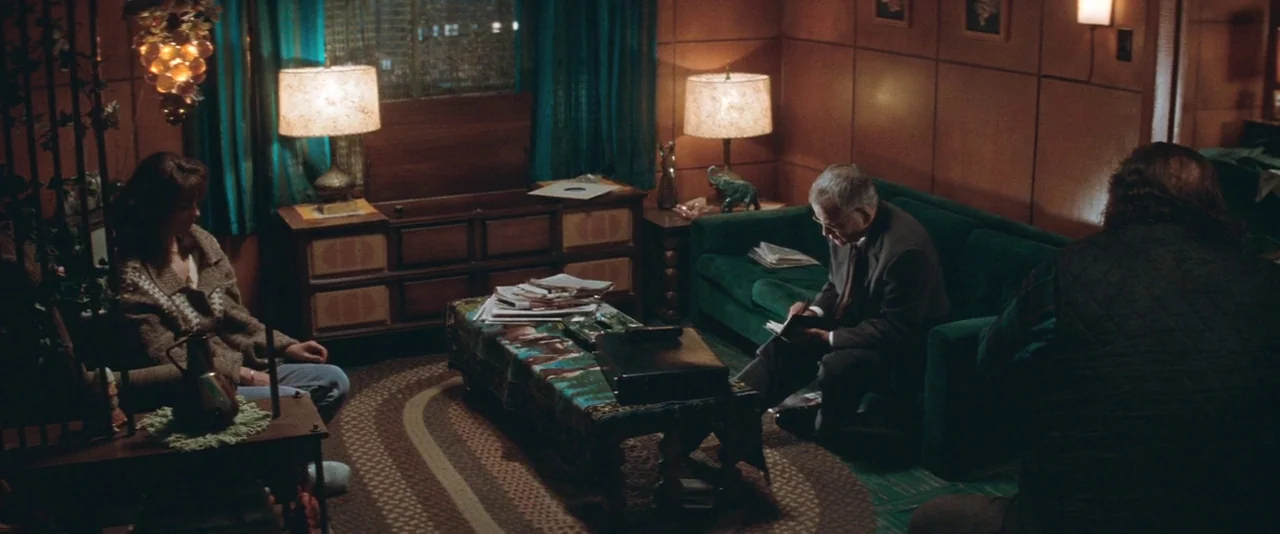 The Sweet Hereafter (1997) movie still: wide — A wood-paneled room features a green velvet sofa and matching shag carpet flooring. An older man sits…