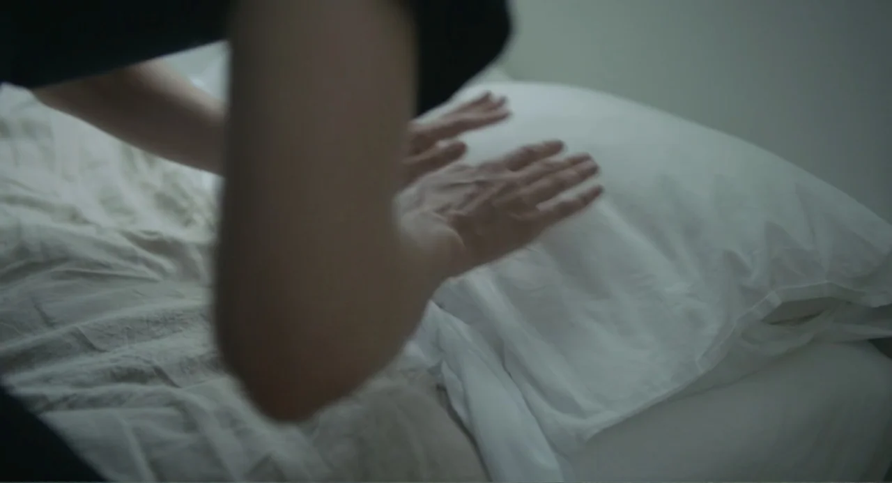 This Closeness (2024) movie still: closeup — A sterile bedroom environment features a white pillow resting on a rumpled white sheet. A person…