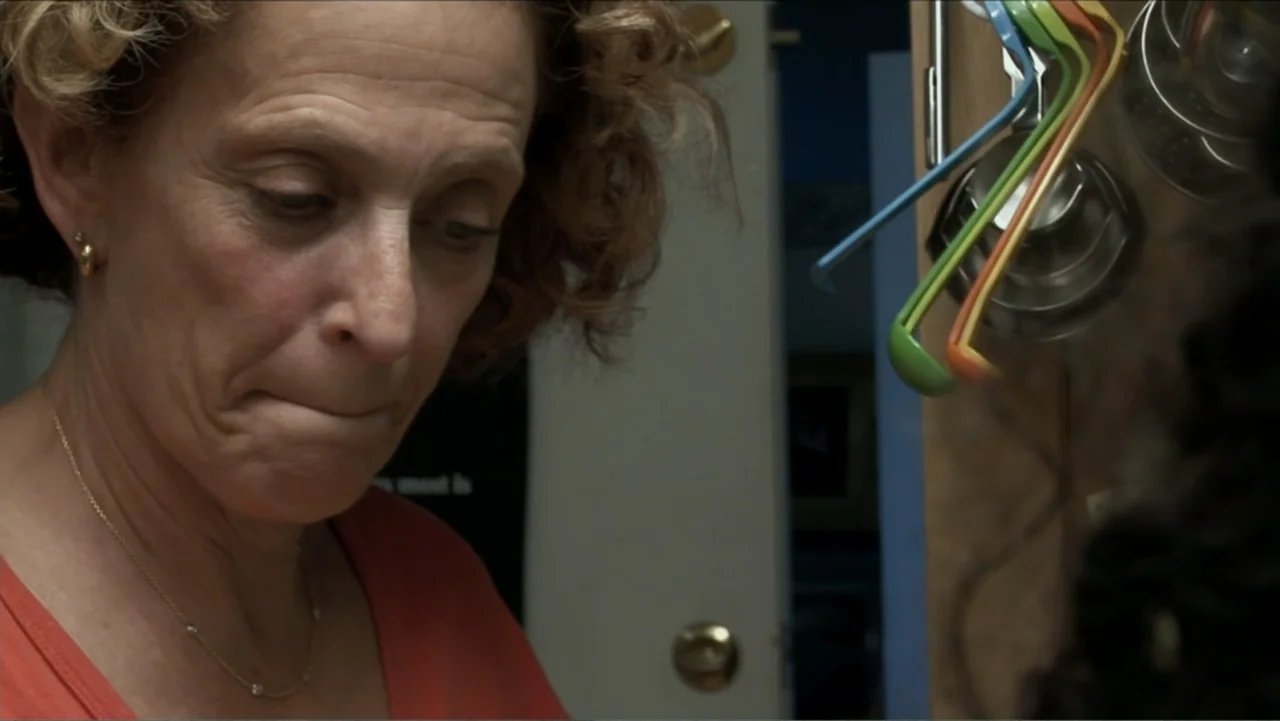 Little White Lie (2008) movie still: closeup — A residential kitchen interior features hanging plastic measuring spoons on a wooden cabinet door. A…