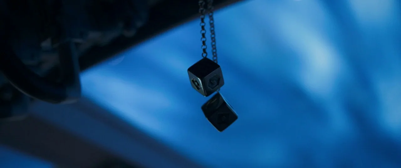 Solo: A Star Wars Story (2018) movie still: closeup — Two metallic cubes hang from a chain against a dark blue blurred background. The object is…