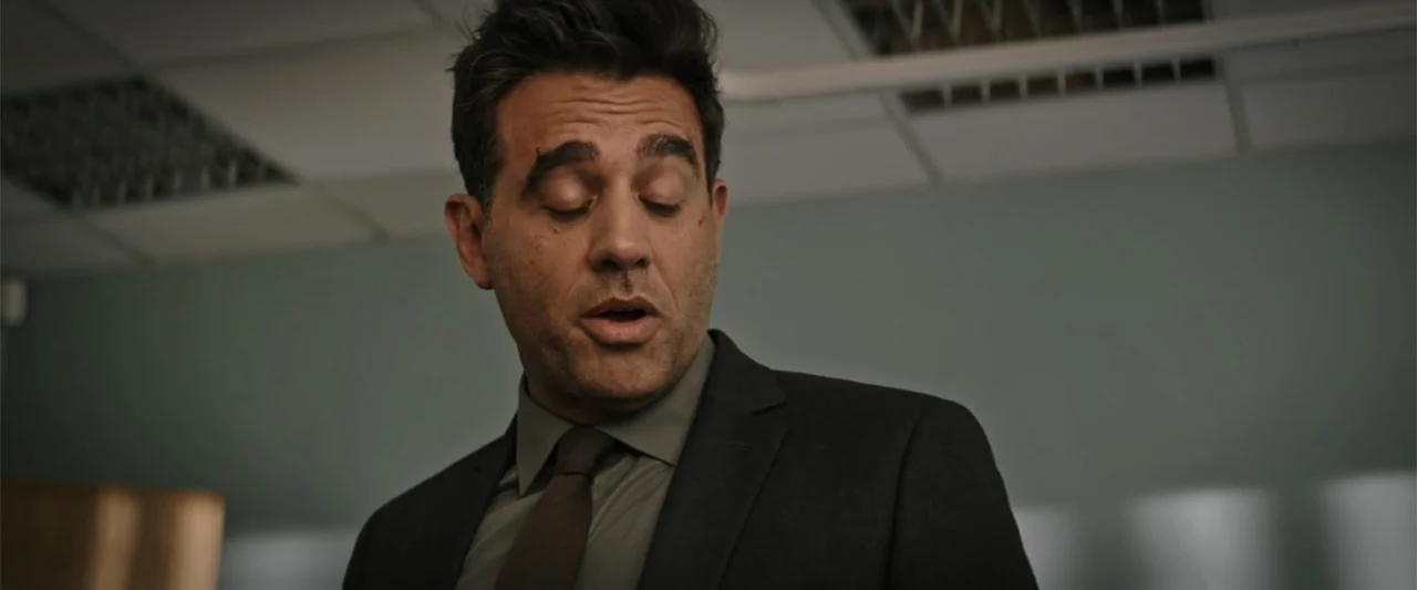 Jolt (2021) movie still: medium — An office environment with muted green walls and visible ceiling fluorescent light panel fixtures. A middle-aged…