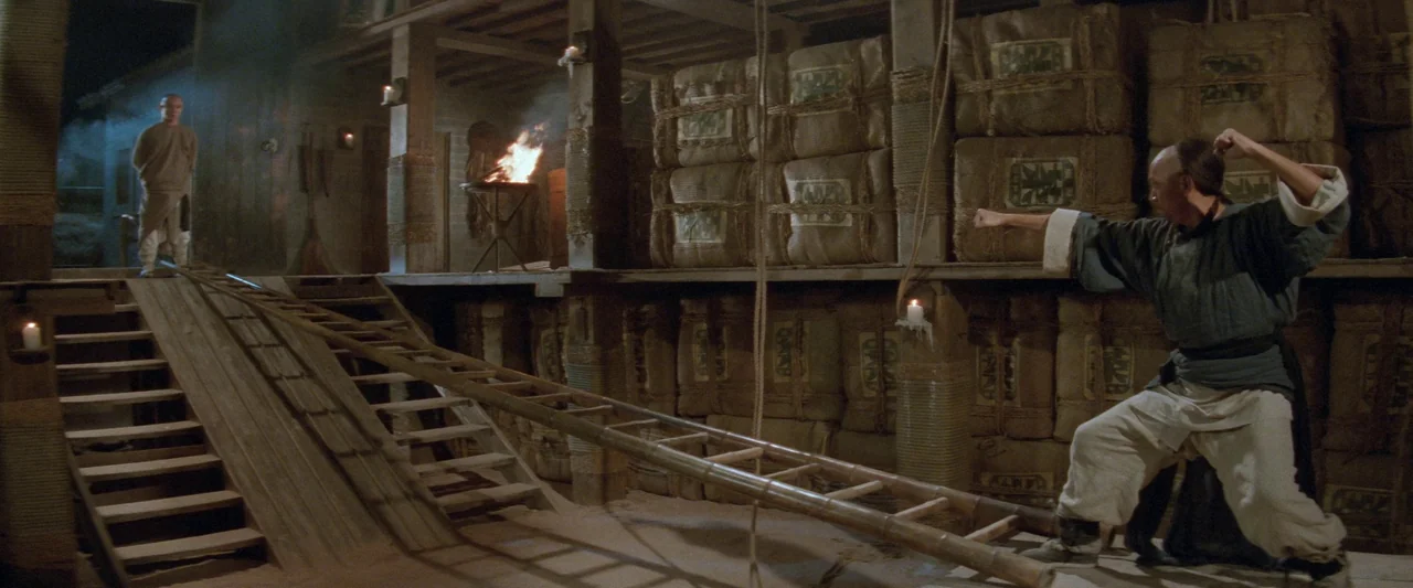 Once Upon a Time in China (1991) movie still: wide — A dark, wooden storage space is filled with stacked burlap sacks and timber supports. Two men…