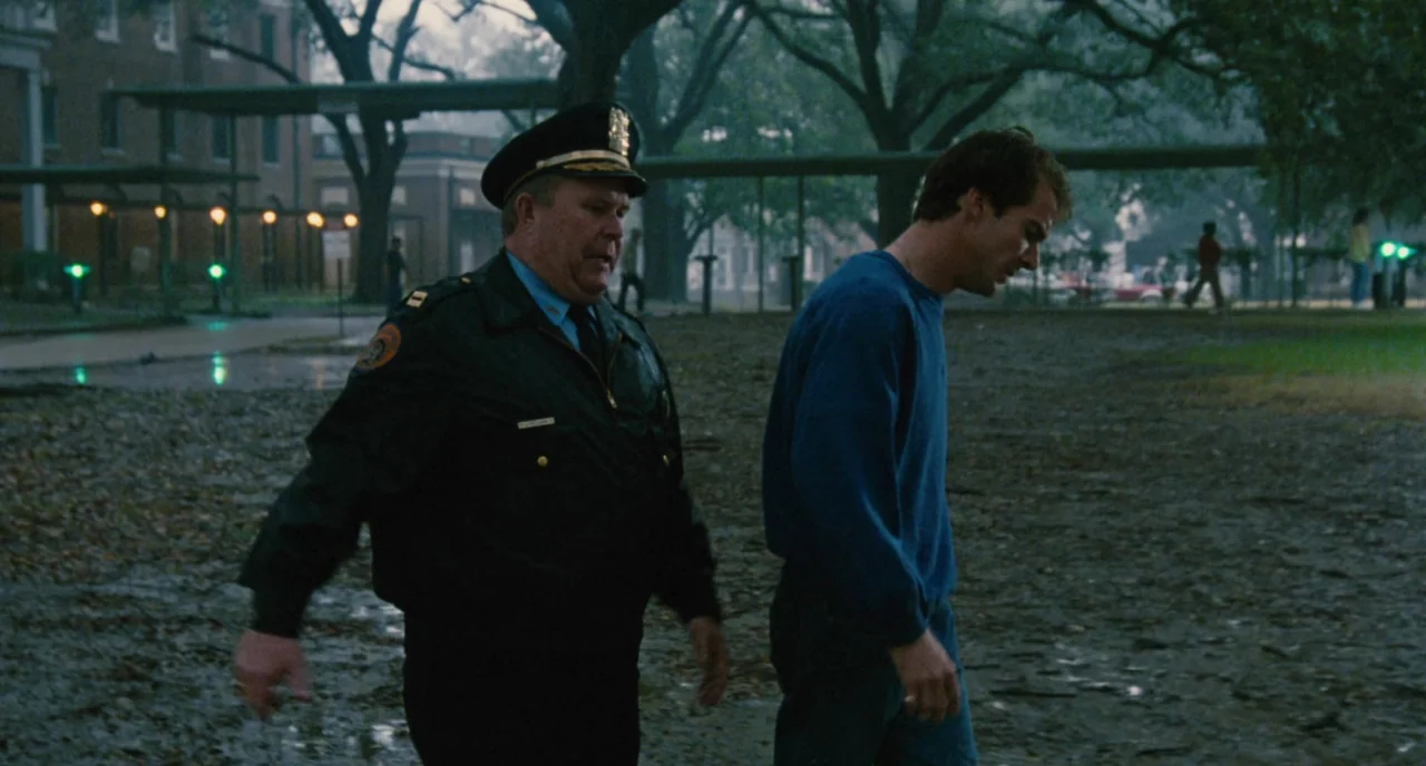 The Big Easy (1986) movie still: medium — A wet, leaf-covered park path at night near a large brick building exterior. A uniformed police officer…