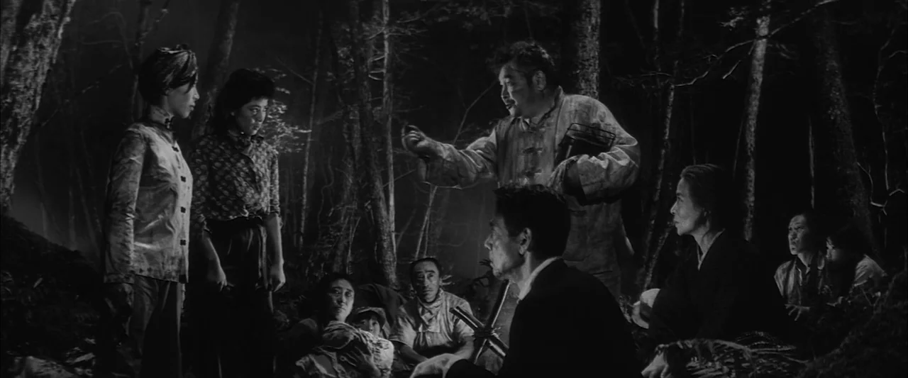The Human Condition III: A Soldier’s Prayer (1961) movie still: fullbody — A group of people gathers in a dark, dense forest at night. An older man…