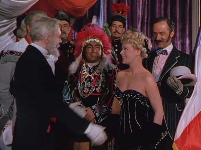 Annie Get Your Gun (1950) movie still: medium — An indoor reception hall with draped curtains and multiple people dressed in formal attire. A woman…