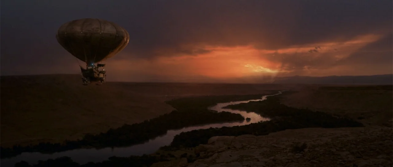 The Mummy Returns (2001) movie still: wide — A wide view of a river valley at golden hour with distant mesas. A large hot air balloon drifts through…