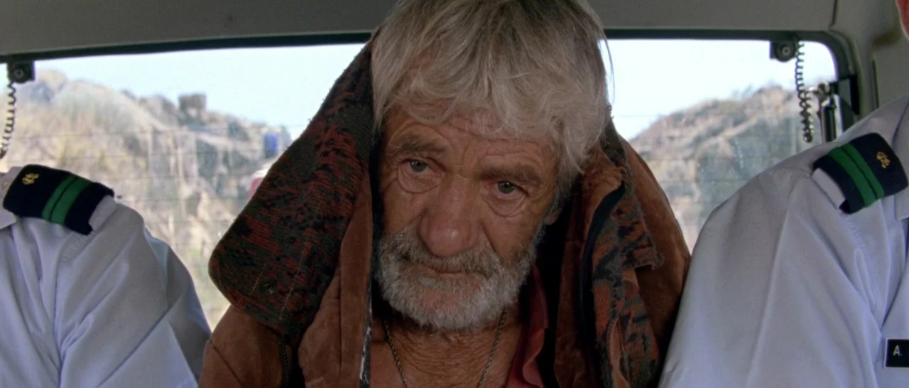 Arabian Nights: Volume 2 The Desolate One (2015) movie still: medium — Inside a vehicle, an older man sits positioned between two uniformed…