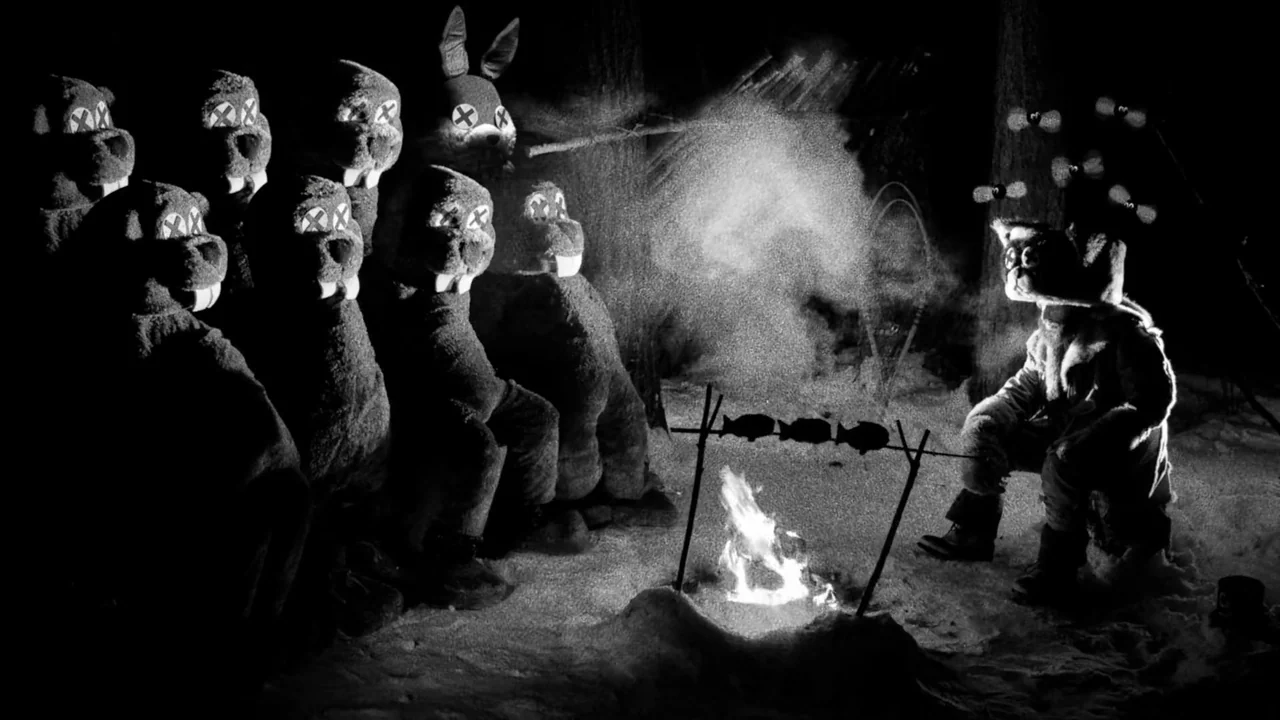 Hundreds of Beavers (2022) movie still: wide — A snowy wooded area at night is illuminated by a crackling campfire. Several figures wearing…
