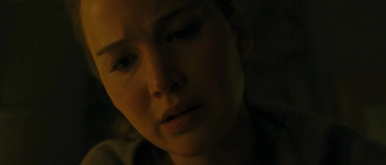 mother! (2017) movie still: closeup — A dimly lit room interior features a person viewed in extreme close-up. The person gazes downward in a…