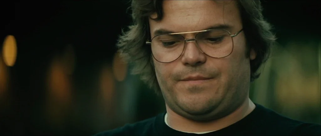 Be Kind Rewind (2008) movie still: closeup — A man with glasses stands in a dark, outdoor setting at night. He stares downward while the background…