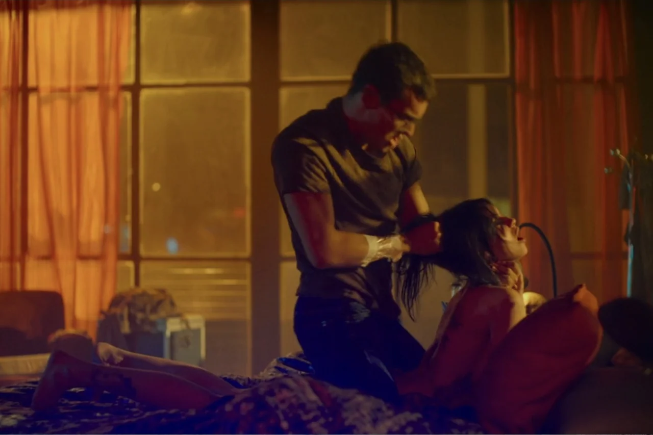 Cross the Line (2020) movie still: medium — A dimly lit bedroom features large window panes with orange curtains against a night sky. A man kneels…