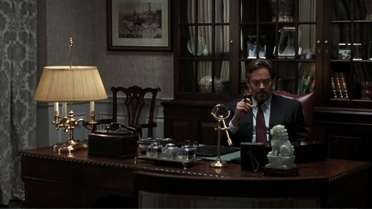 Presumed Innocent (1990) movie still: medium — A wood-paneled study features a large mahogany desk and a tall glass-fronted bookcase. A man in a…