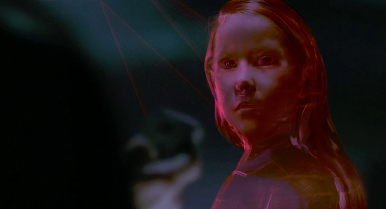 Resident Evil (2002) movie still: closeup — A dark, featureless environment contains a glowing, red, semi-transparent holographic projection of a…