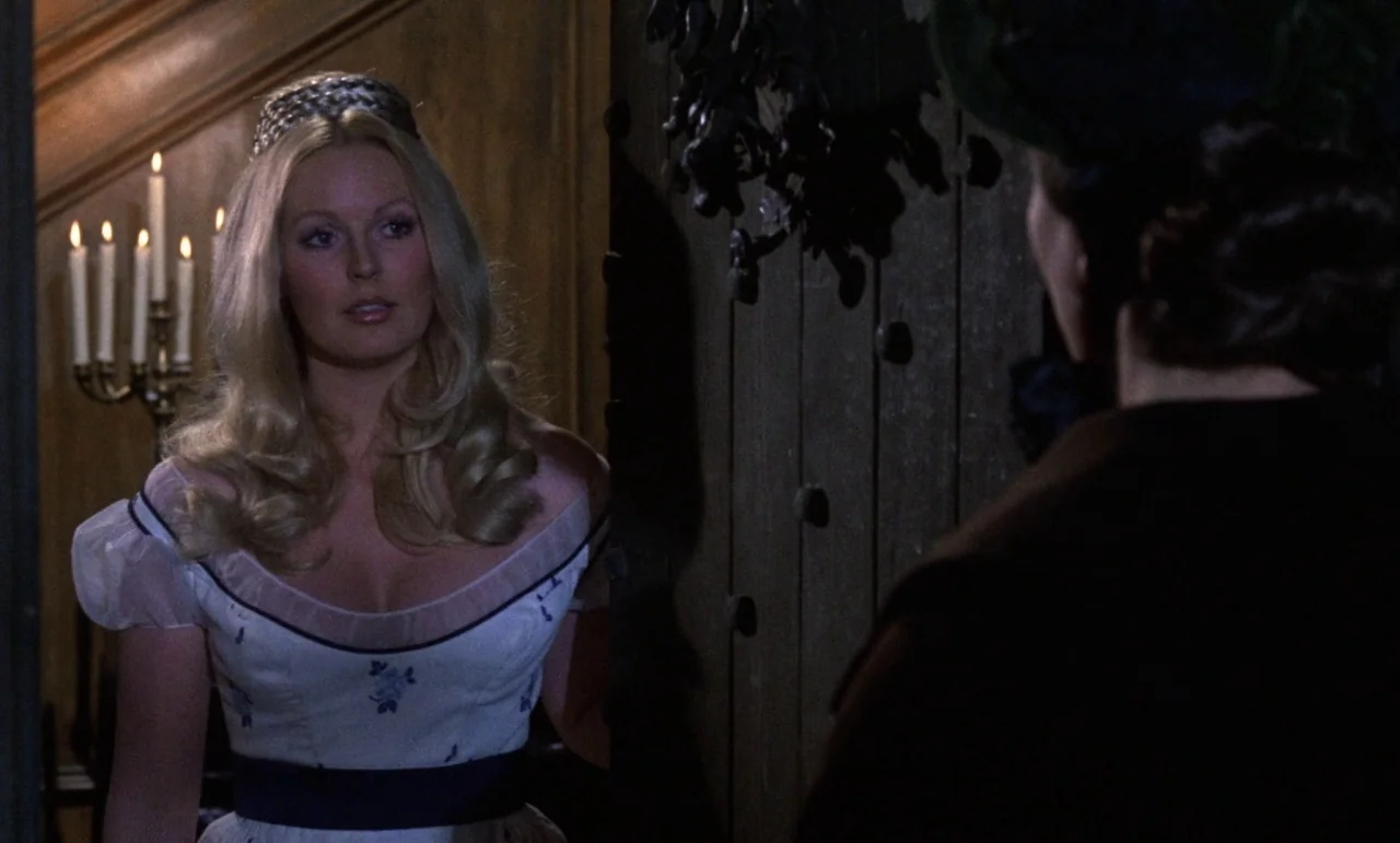 The Horror of Frankenstein (1970) movie still: medium — A dimly lit wooden doorway frames a woman standing in a hallway. The space is accented by a…
