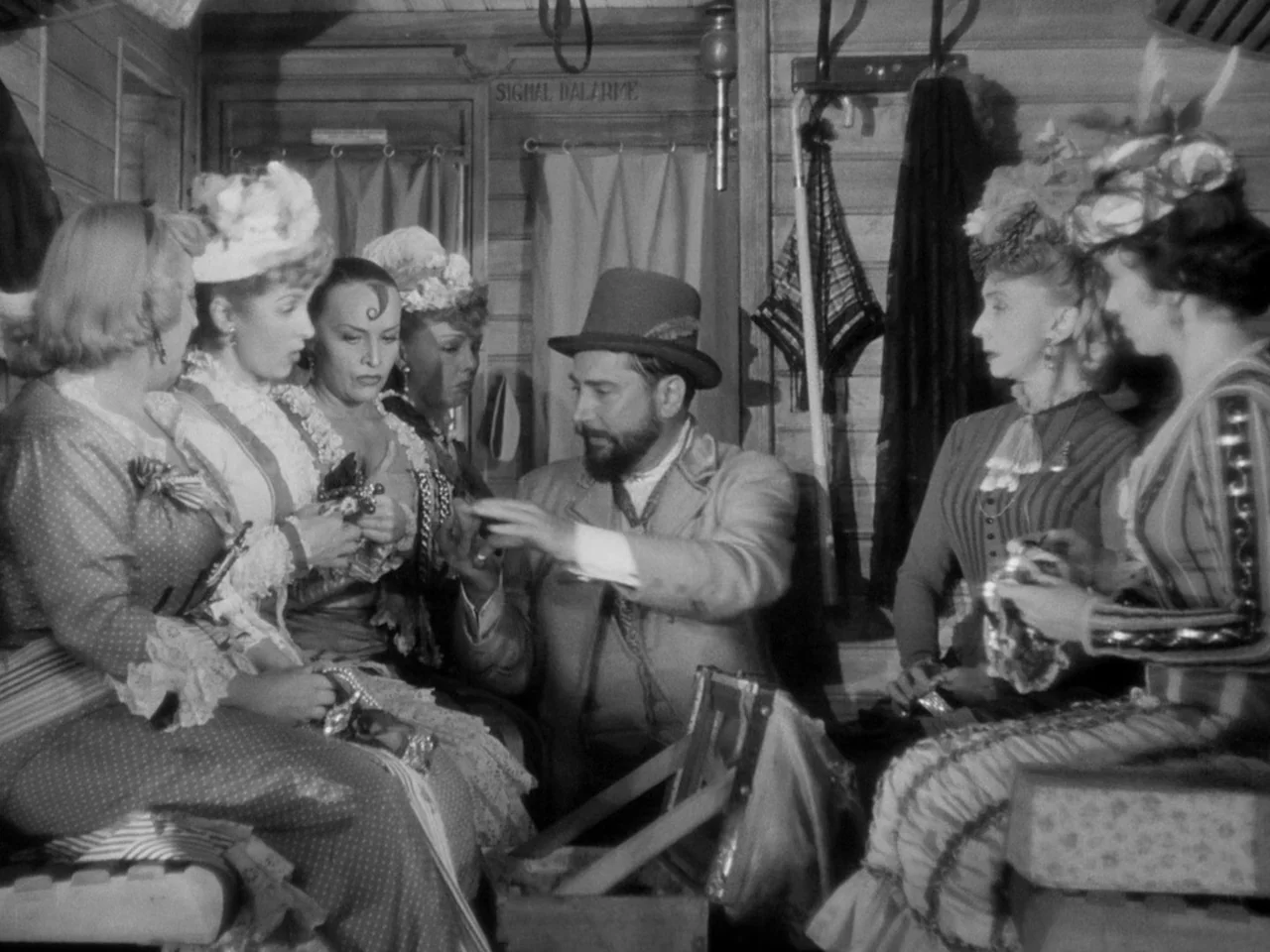 Le Plaisir (1952) movie still: medium — A vintage wooden train interior features horizontal planks, small curtains, and hanging garment hooks. A…