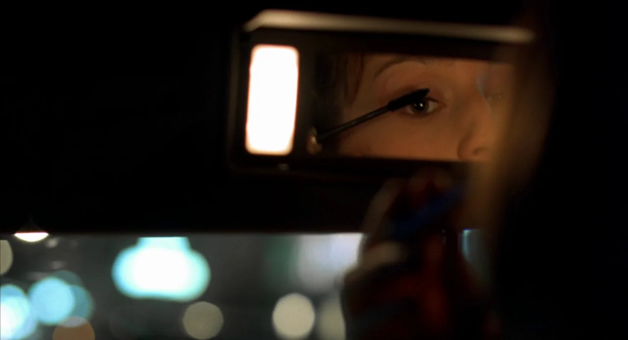 The Good Thief (2002) movie still: closeup — A dark car interior at night shows a woman's eyes reflected in a vanity mirror. She uses a mascara wand…