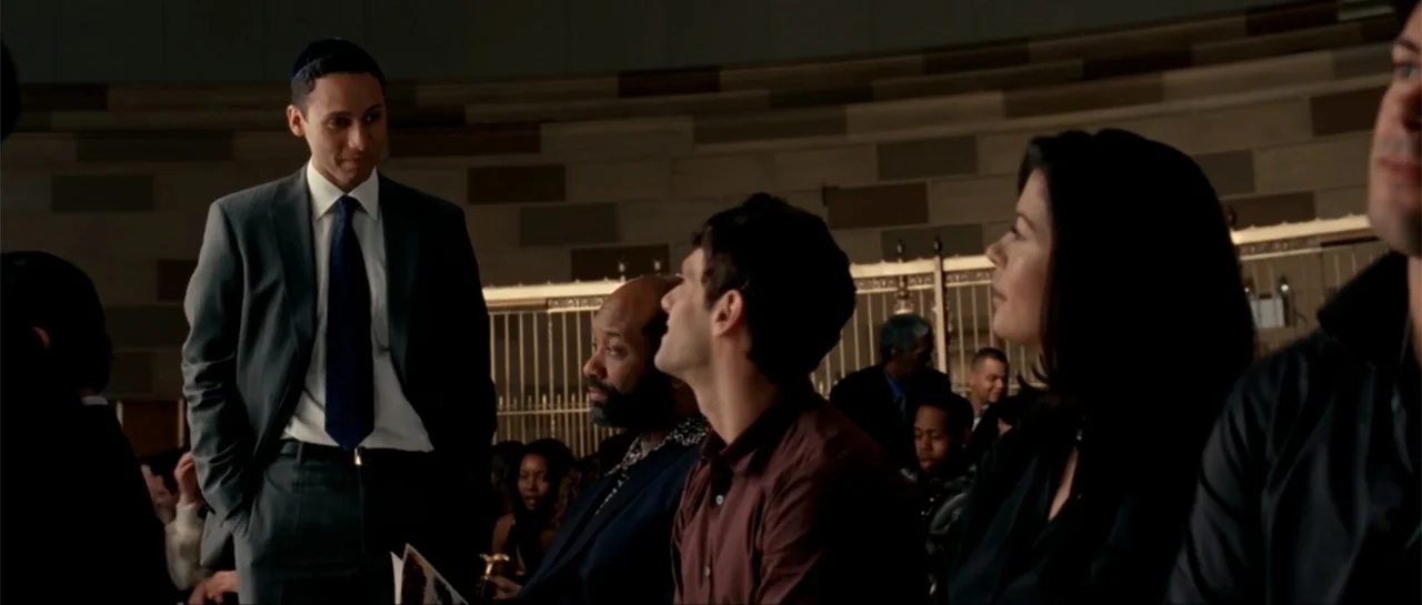 The Rebound (2009) movie still: medium — A spacious auditorium interior with tiered seating and a metal railing in the background. A man in a suit…