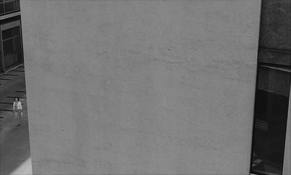 La Notte (1961) movie still: wide — A monolithic, smooth concrete facade occupies the majority of the frame. A single woman walks on the pavement…
