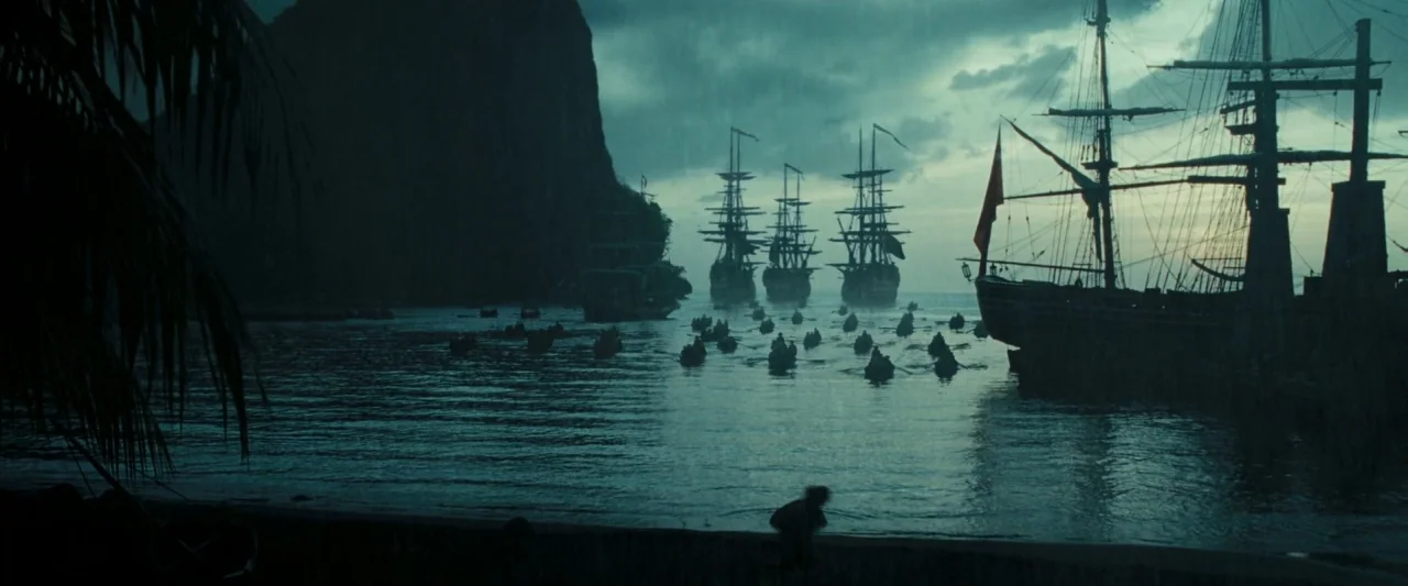 Pirates of the Caribbean: Dead Man’s Chest movie still: wide — A dark tropical bay features large masted ships anchored beneath a towering rocky…