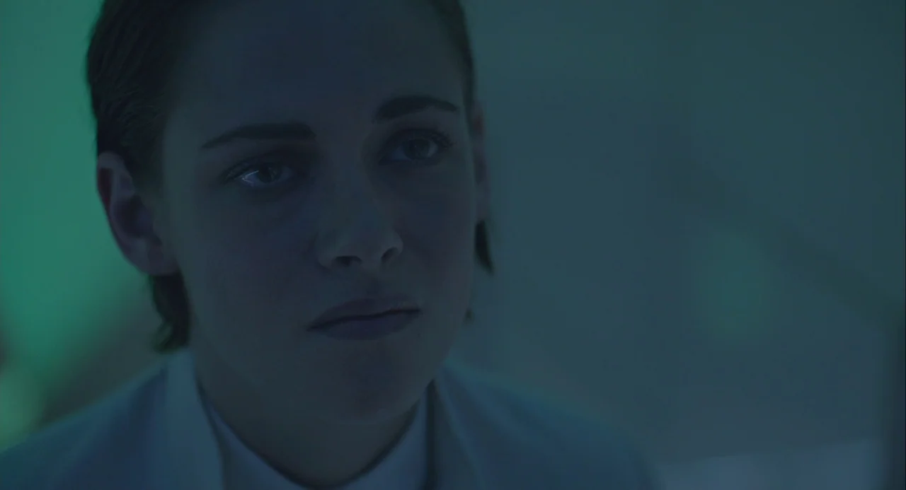 Equals (2015) movie still: closeup — A dimly lit interior space with cool cyan tones and soft ambient illumination. A woman stares toward the side…