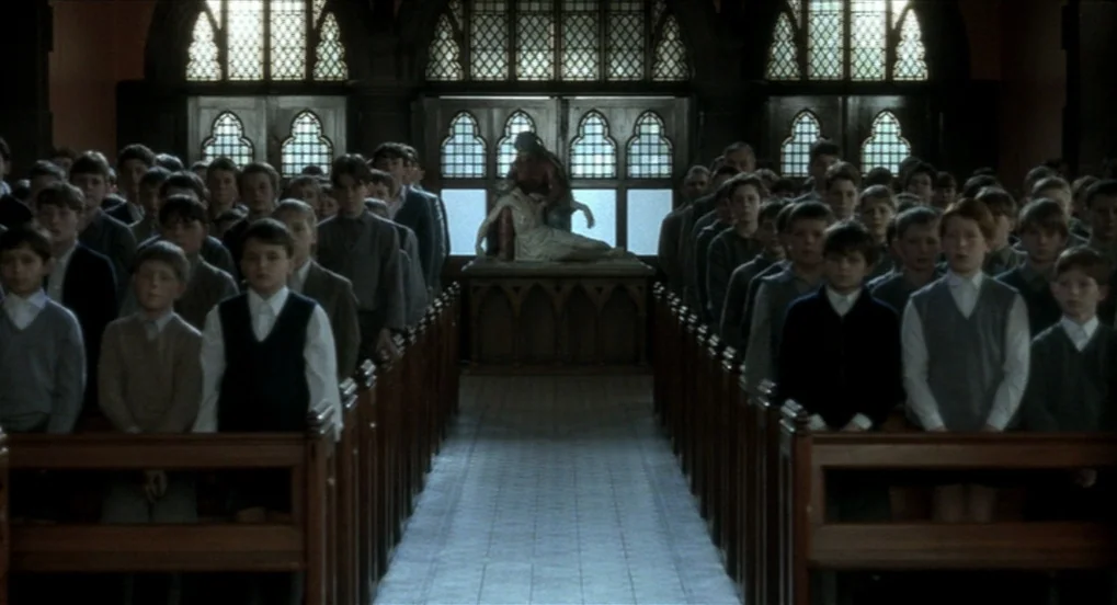 The Long Day Closes (1992) movie still: wide — A long aisle of a church contains rows of young schoolboys sitting in pews. At the far end stands a…