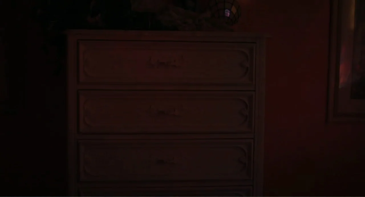 Ted Bundy: American Boogeyman (2021) movie still: medium — A dark, dimly lit wooden dresser stands against a deep red wall. There are no occupants…