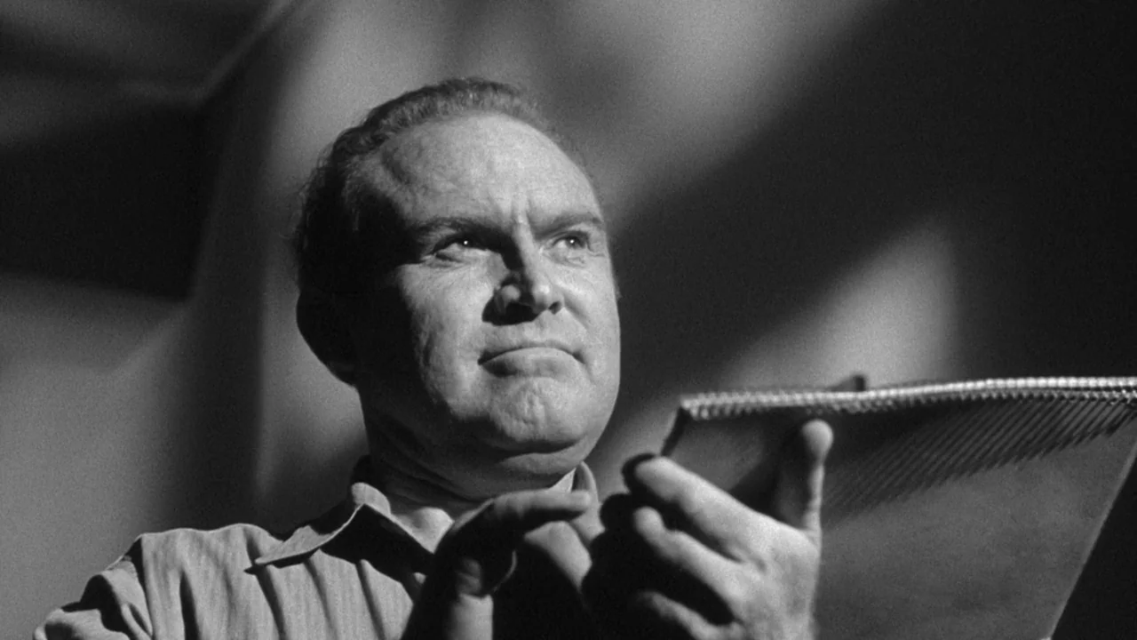 Shock Corridor (1963) movie still: closeup — An interior space features a man positioned against a shadowed, textured background. The subject holds…