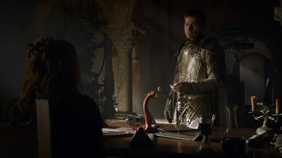 Game of Thrones (2015) movie still: medium — A dark stone hall with high ceilings and architectural columns features a central table. A man in metal…
