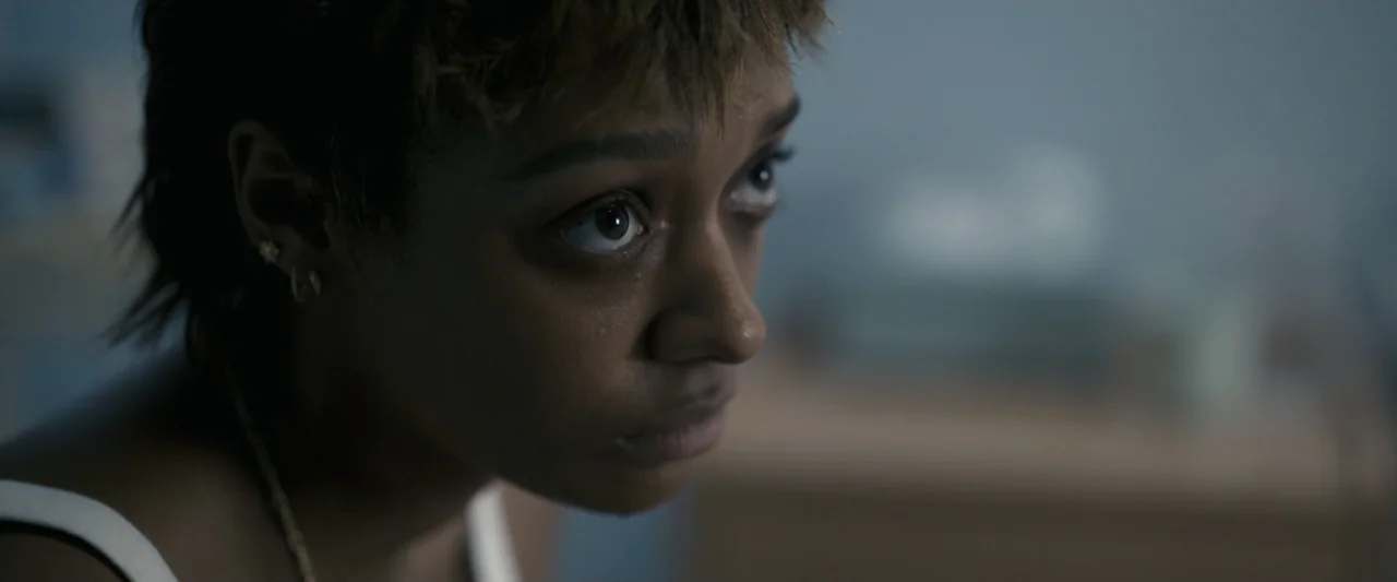 Talk to Me (2023) movie still: closeup — A close view of a young woman's face inside a dark bedroom environment. She gazes past the camera lens into…
